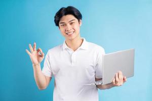 Hombre asiático sosteniendo su computadora portátil y mostrando el símbolo ok en la mano foto
