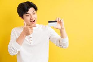 Asian man holding a bank card in his hand on a yellow background
