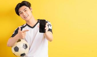 el hombre asiático está sosteniendo una pelota y apuntando al teléfono con una pantalla en blanco foto