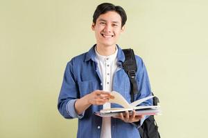 Foto de guapo estudiante asiático sonriendo y sosteniendo el libro en la mano
