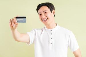 Apuesto hombre de negocios asiático sonriendo y mirando la tarjeta de crédito en su mano foto