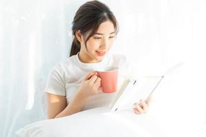 Retrato de una joven asiática leyendo un libro y tomando café foto