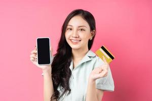 Joven mujer asiática sosteniendo un teléfono móvil mientras sostiene una tarjeta bancaria en la mano foto