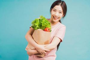 Young girl holding a bag of freshly bought vegetables on a green background