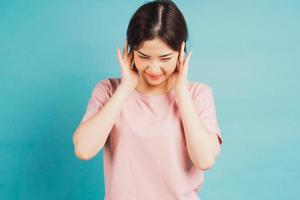Portrait of girl covering ears and feeling discomfort on blue background photo