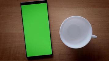 Vista superior de una mano masculina prepara café instantáneo en una taza blanca cerca de un teléfono con pantalla verde video