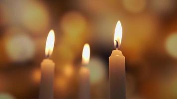 Close-up of three candles burning over a background of colored blurred bokeh video