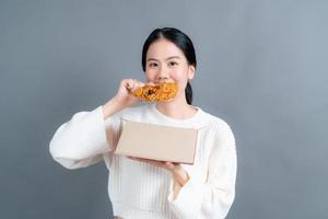 Young Asian woman wearing a sweater with a happy face and enjoy eating fried chicken on grey background photo