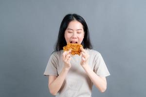 Joven asiática vistiendo un suéter con una cara feliz y disfruta comiendo pollo frito sobre fondo gris foto