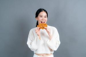 Young Asian woman wearing a sweater with a happy face and enjoy eating fried chicken on grey background photo