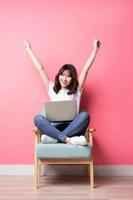 Asian woman sitting on sofa using laptop with happy expression