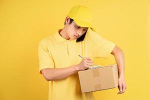 Retrato de hombre de entrega sosteniendo la caja de carga y usando el teléfono sobre fondo amarillo foto