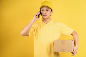 Retrato de hombre de entrega sosteniendo la caja de carga y escuchando el teléfono sobre fondo amarillo foto