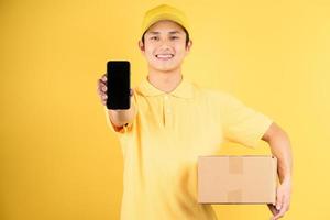 Entrega retrato masculino sosteniendo la caja de carga y sosteniendo el teléfono hacia adelante sobre fondo amarillo foto