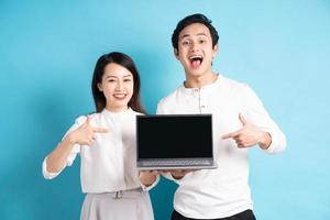 Portrait of happy young couple using laptop on blue background photo