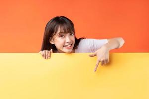 Young Asian girl pointing her finger down on yellow and orange background photo