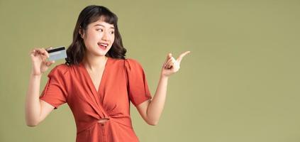 Mujer asiática sosteniendo una tarjeta bancaria y apuntando su dedo hacia la izquierda