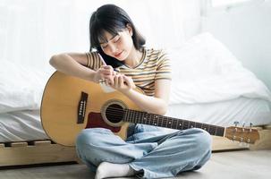 Joven asiática está practicando guitarra en casa y componiendo música foto