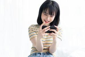 Beautiful Asian woman playing game on smart phone in bedroom photo