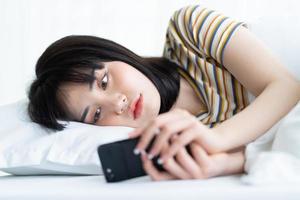 Beautiful Asian woman using phone on bed in bedroom