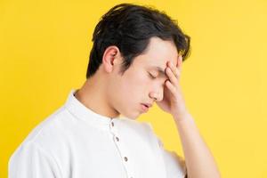 Portrait of young man having a headache on a yellow background photo