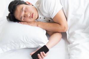 The young man is sleeping on the bed with the phone still in his hand photo