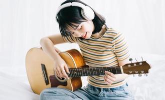 Joven asiática está practicando guitarra en casa y componiendo música foto