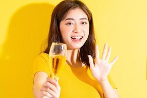 Young Asian woman drinking wine and posing on yellow background photo