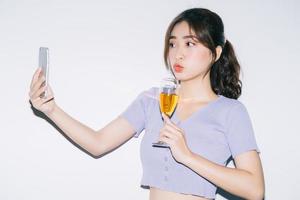 Joven mujer asiática bebiendo vino y con smartphone sobre fondo blanco. foto
