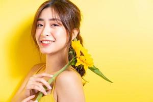 Beautiful Asian woman holding and posing with sunflower on yellow background photo