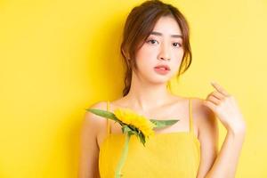 Hermosa mujer asiática sosteniendo y posando con girasol sobre fondo amarillo foto