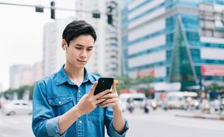 Joven asiático caminando y usando el teléfono inteligente en la calle foto