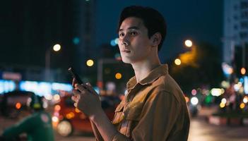 Joven asiático está usando su teléfono mientras camina en la calle por la noche foto