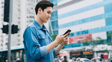 Joven asiático caminando y usando el teléfono inteligente en la calle foto