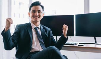 La empresaria asiática está sonriendo con confianza junto a dos pantallas de ordenador en blanco foto