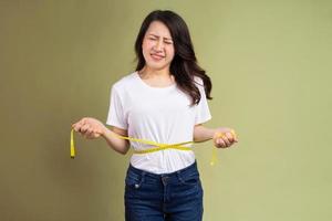 Joven asiática sosteniendo una cinta métrica molesta por el aumento de peso