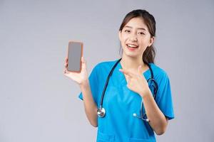 Young Asian doctor with smartphone on grey background photo