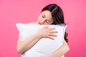 La mujer asiática está abrazando la almohada sobre fondo rosa