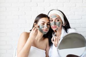 Dos hermosas mujeres aplicando mascarilla facial divirtiéndose foto