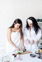 Dos hermosas mujeres haciendo procedimientos de spa cortando pepinos foto