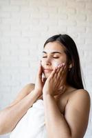 Happy beautiful woman wearing bath robes applying facial cream on her face photo