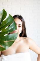 Happy beautiful woman wearing bath towels holding a green monstera leaf in front of her face photo