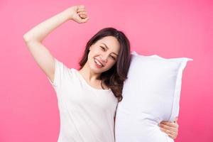 La mujer asiática está abrazando la almohada sobre fondo rosa