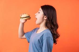 Young Asian woman eating hamburger on orange background photo