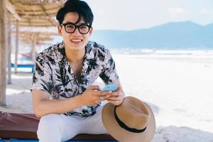 Young Asian man using smartphone on the beach