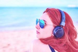 hermosa mujer con gafas de sol escuchando música en la playa. foto