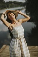 Relaxing young woman standing on wooden pier at the lake photo