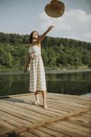 Happy young woman standing on wooden pier at the lake photo