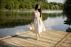 Relaxing young woman standing on wooden pier at the lake photo