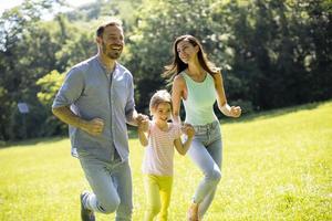 Happy young family with cute little daughter running in the park on a sunny day
